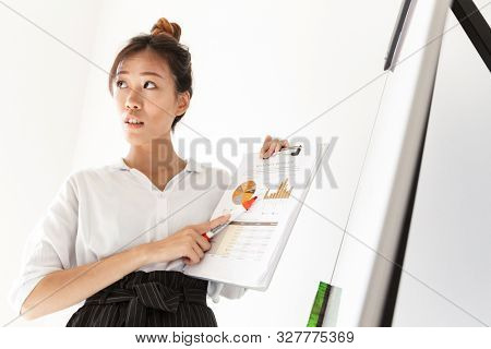 Attractive confident asian businesswoman presenting new project at the blankboard isolated over white background