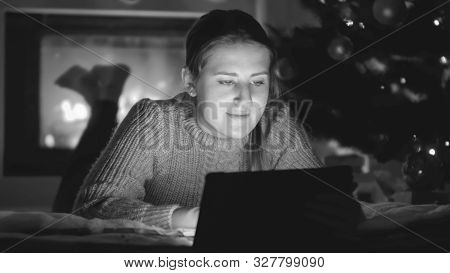 Black And White Portrait Of Young Woman Lying On Floor Next To Firepalce And Browsing Internet On Di