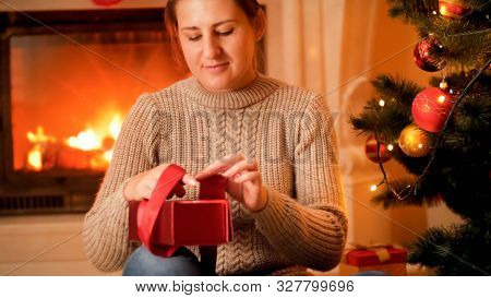 Portrait Of Young Woman In Sweater Sitting Next To Burning Firepalce And Packing Christmas Gifts And