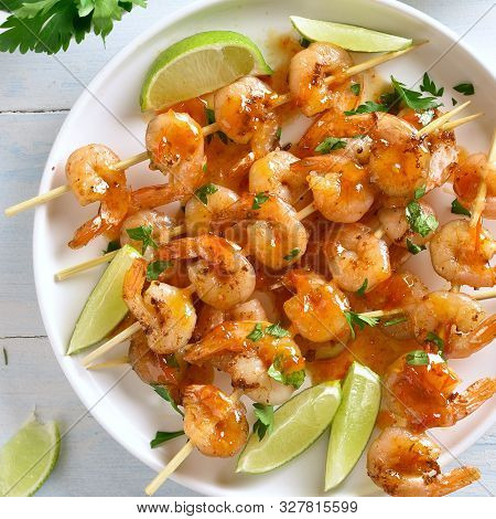 Prawns Skewers With Greens, Spices, Lime And Sauce On White Plate Over Wooden Table. Grilled Shrimp 
