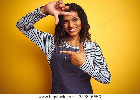 Young transsexual transgender chef woman wearing apron over isolated yellow background smiling making frame with hands and fingers with happy face. Creativity and photography concept.