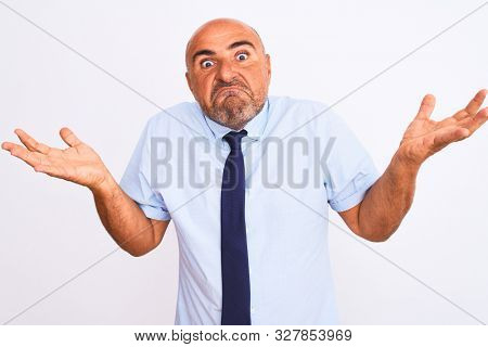 Middle age businessman wearing tie standing over isolated white background clueless and confused expression with arms and hands raised. Doubt concept.
