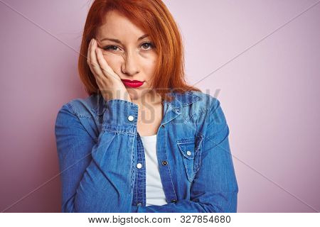 Youg beautiful redhead woman wearing denim shirt standing over isolated pink background thinking looking tired and bored with depression problems with crossed arms.