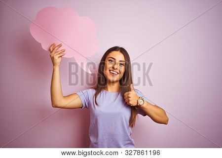 Young beautiful woman holding cloud speech bubble over isolated pink background happy with big smile doing ok sign, thumb up with fingers, excellent sign