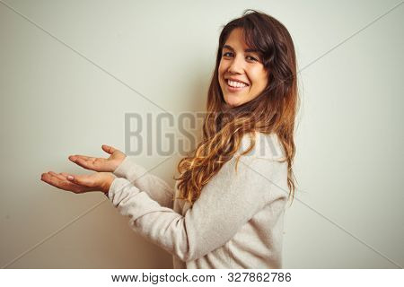Young beautiful woman wearing winter sweater standing over white isolated background pointing aside with hands open palms showing copy space, presenting advertisement smiling excited happy