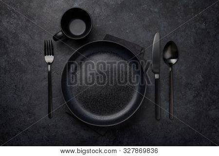 Empty plate, cup, fork and knife. Black kitchen utensils set on stone table. Top view flat lay with copy space