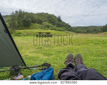Iceland, Landmannalaugar, August 2, 2019: Hikers Legs In Hiking Boots At Green Tent In Camping Site 
