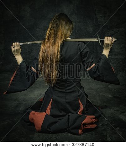 Full Length Portrait Of Young Long Haired Woman Wearing A Medieval Costume. Siting Pose With A Sword