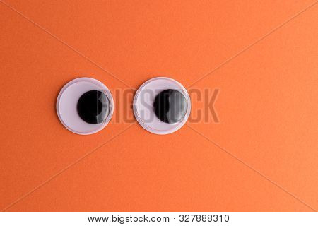 Googly Eyes On Orange Background. Minimal Holiday Concept.