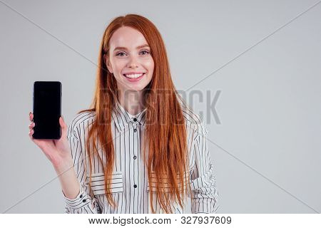 Cheerful Redheared Woman Businesswomen In A Striped Shirt Showing Blank Smartphone Screen White Back