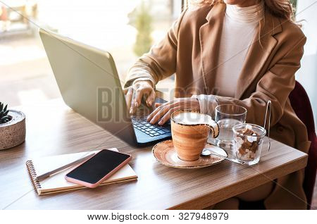Beautiful Business Woman Sitting In Cafe Andworking. There Are Laptop, Smartphone And Cup Of Coffee.