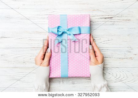 Top View Woman Hands Holding Present Box With Colored Bow On White Rustic Wooden Background With Cop