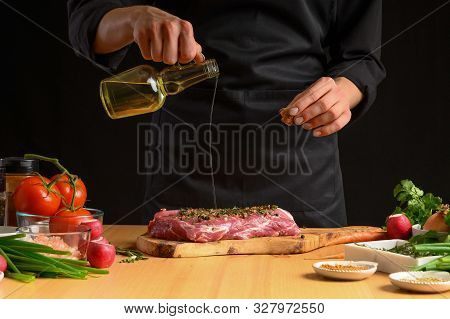 Chef Cooks Pork Steak. Pouring Oil On The Background With Vegeta