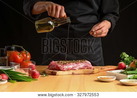 Chef Cooks Pork Steak. Pouring Oil On The Background With Vegeta