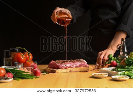 Chef Cooks Pork Steak. Pouring Sauce, Marinade On A Background W