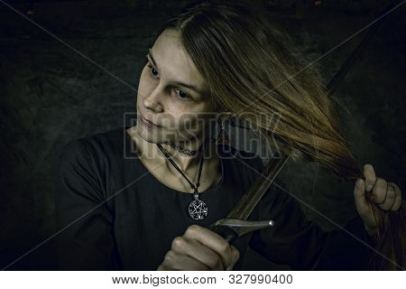 Portrait Of Young Long Haired Woman Wearing A Medieval Costume. Standing Pose With A Sword At Her Ha