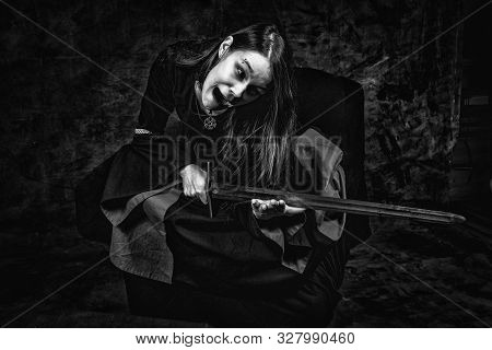 Portrait Of Young Long Haired Woman Wearing A Medieval Costume. Sitting Pose Scratching Her Hand Wit