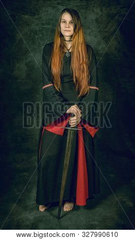 Full Length Portrait Of Young Long Haired Woman Wearing A Medieval Costume. Standing Pose With A Swo