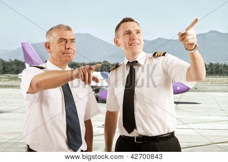 Munter to piloter, iført uniform med skulderpuder stående på landingsbanen og peger på som