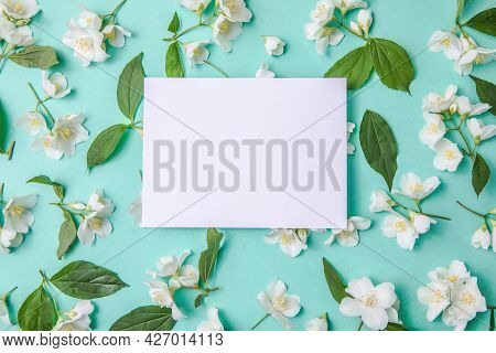 Composition Of Green Leaves And Flowers Of Jasmine  With A Blank Sheet For Text On A Green  Paper Ba