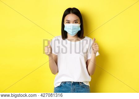 Covid-19, Quarantine And Social Distancing Concept. Cheerful Asian Woman In Medical Mask And White T