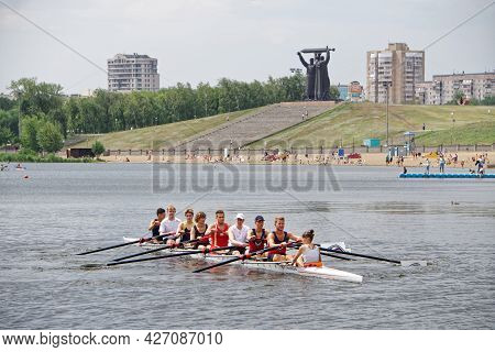 Kayak With Eight Rowers On The Surface Of The Ural River, Near The City Beach And The Tyl Front Monu