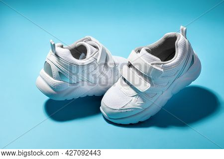 Two White Teen Hovering In The Air Running Shoes Isolated On A Blue Background With Hard Shadows