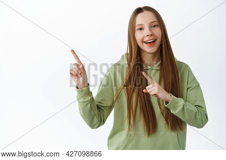 Looh This Way. Smiling Teen Girl Demonstrate Logo, Pointing At Banner, Showing Promo Aside, Standing