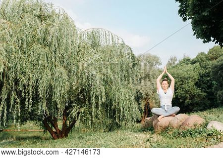 Young Woman Practicing Meditation Sitting On Stones And Doing Yoga Pose Parvatasana Enjoying The Mor