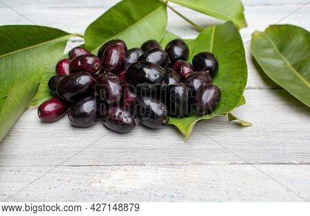 Stack Of Organic Jamun Or Black Plum Isolated On Wooden Background With Leaves, Also Known As Syzygi
