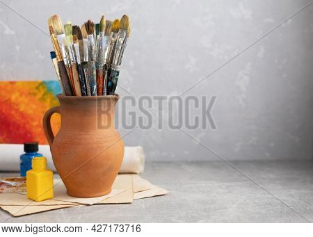 Paint brush in clay jug and art painter tool on table background texture. Paintbrush for painting as artistic paint still life. Abstract art concept