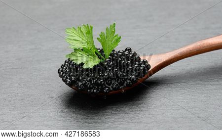 Fresh Grainy Black Paddlefish Caviar In Brown Wooden Spoon On A Black Background, Close Up