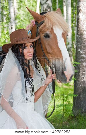Jovem mulher com o vestido de noiva ao lado de um cavalo por um dia Canicular em uma madeira de vidoeiro