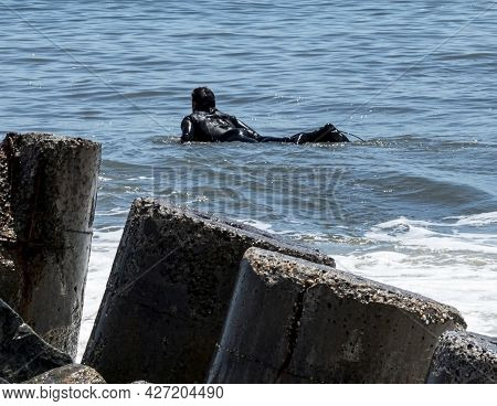 A Man Is Lying On His Surfboard Next To A Jetty Wearing A Black Wetsuit Waiting For A Wae To Ride
