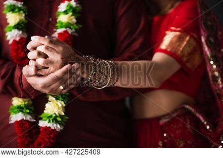 Cropped View Of Indian Man In Floral Garland Holding Hands With Bride In Traditional Sari