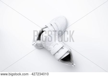 Top View On A Pyramid Of White Child Sneakers, One Sneaker Lies On Another Sneaker Isolated On A Whi