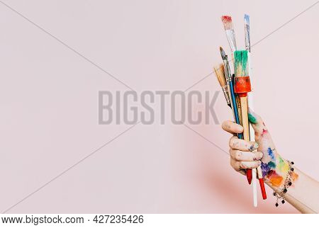 Creative Background. Female Artist Hand Holding Colorful Paintbrushes. Paints And Brushes Background