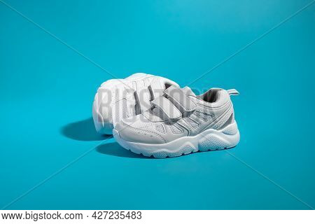 One White Kid Sneaker With Velcro Fasteners For Easy Shoeing Stands In Front Of The Other Lying On I