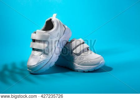 Front View Of A Composition Of White Childrens Sneakers On A Blue Background With Shadows From A Pal