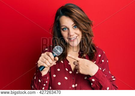 Young caucasian woman singing song using microphone smiling happy pointing with hand and finger 