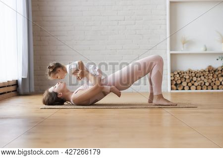 Woman And Her Charming Little Daughter Are Smiling While Doing Yoga Together At Home. Young Smiling 