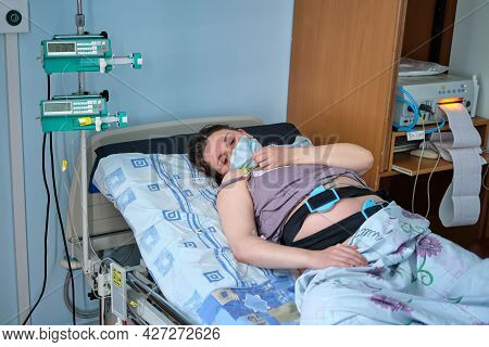 A Pregnant Woman In Medical Mask Gives Birth In A Hospital With A Drip And A Ctg Machine. A Woman On