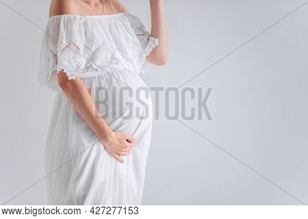Close-up A Young Pregnant Woman In Anticipation Of A Baby In A White Hat, Dress, Hugs Her Belly. Ten