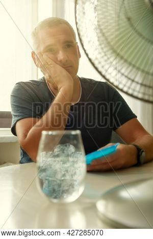 Man suffers from heat while sitting in the oom and tries to cool off by the fan