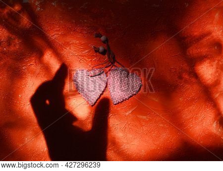 Blurred Shadow Of Female Hand And Two Wooden Heart On Rough Red Wall Background. Sunlight And  Cross