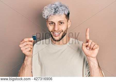 Young hispanic man with modern dyed hair holding sdxc card surprised with an idea or question pointing finger with happy face, number one 