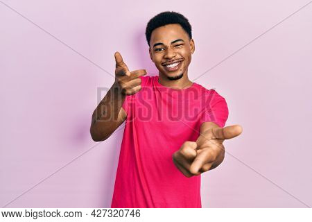 Young african american man wearing casua t shirt pointing fingers to camera with happy and funny face. good energy and vibes. 
