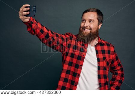 Cheerful And Charismatic European Guy With Beard Talking To Friend Via Internet Messanger App, Holdi