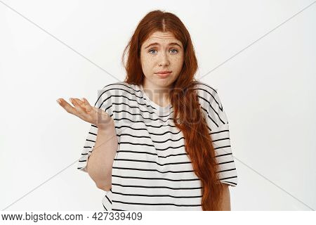 I Dont Know. Clueless Redhead Teenage Girl Shrugging Shoulders And Raise Hand, Looking Confused And 
