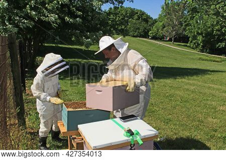 Mother Showing Her Child How To Add Another Hive Box To A Langstroth Beehive With Green Plant Backgr